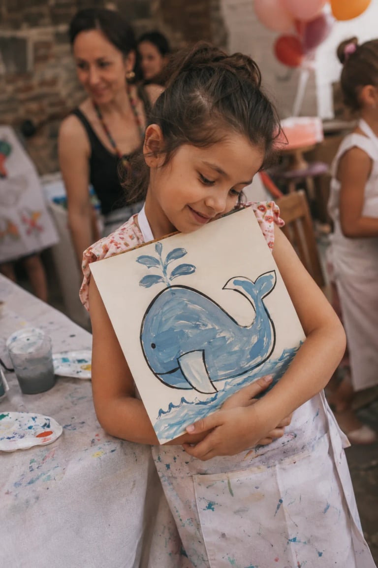 Niña abrazando la pintura de una ballena que creó en el taller